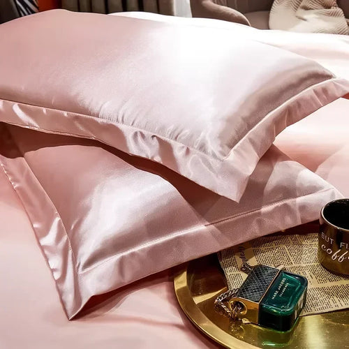 Pink smooth satin-feel pillowcase set folded on a bed