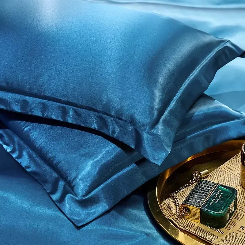 Blue smooth satin-feel pillowcase set stacked on a bed