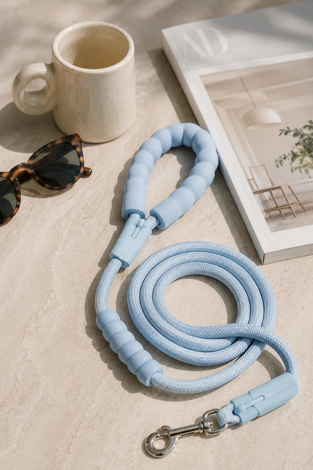 Sky blue rope dog leash with padded handle and metal clasp on a beige surface