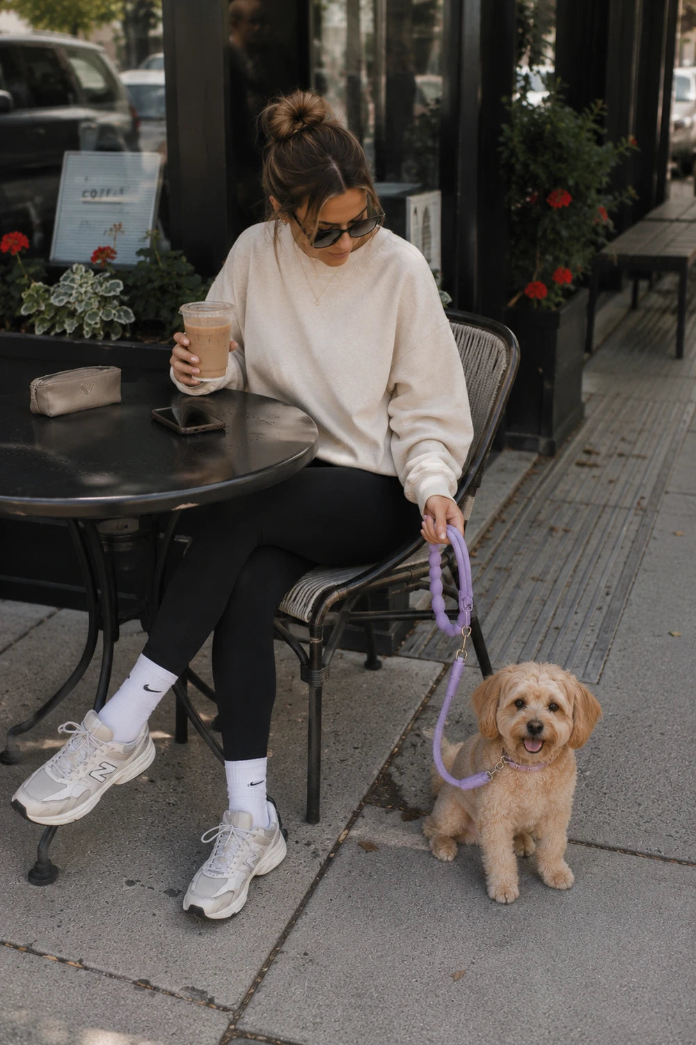 Woman at an outdoor cafe with a small dog on a purple rope leash